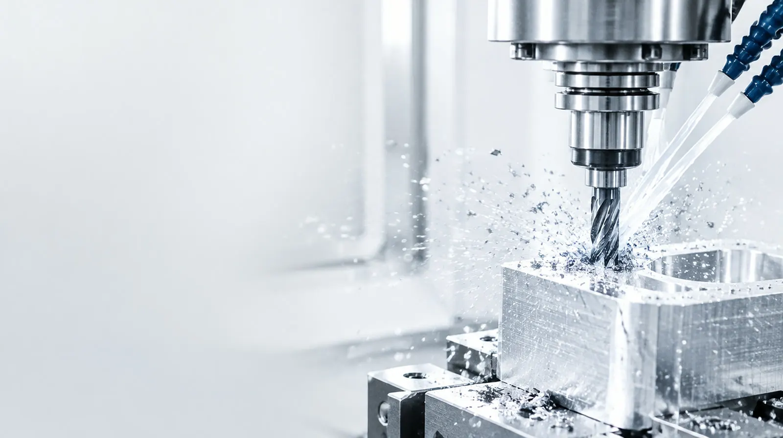 CNC milling cutter machining an aluminium block with metal chips and coolant spray